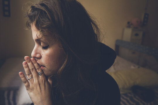 Woman with hands clasped praying at home