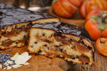 Chocolate bundt or panettone cake decorated chocolate glaze with fruit filling on a wooden brown kitchen boards with persimmon, almonds and grains of chocolate. Shallow depth of field