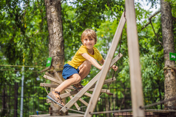 Obraz premium Little boy in a rope park. Active physical recreation of the child in the fresh air in the park. Training for children