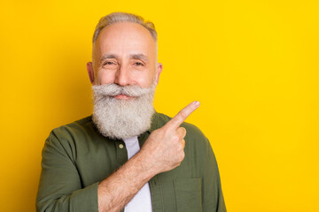 Photo portrait of elder man showing blank space with finger advising isolated vivid yellow color...