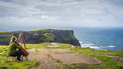 Woman playing harp on the top of iconic Cliffs of Moher, popular tourist attraction, Wild Atlantic...