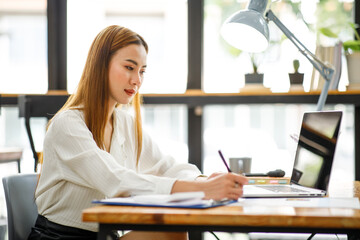 Confident businesswoman documents working on laptop at her workplace at modern office. reading financial report analyzing statistics pointing at pie chart working at her desk.