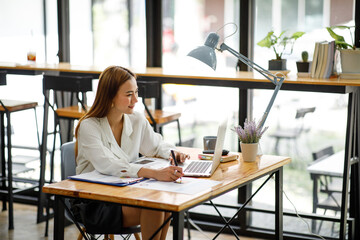 Confident businesswoman documents working on laptop at her workplace at modern office. reading financial report analyzing statistics pointing at pie chart working at her desk.