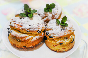 Easter muffins, craffin in white sugar powder, raisins and mint leaves, on a white plate
