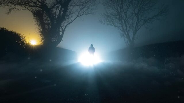 A UFO concept of lights floating in the sky, with a scary, mysterious hooded figure, standing in front of a bright light on a country lane, on a spooky foggy winters night.