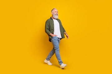 Full length body size side profile photo of senior man smiling walking forward isolated vibrant yellow color background