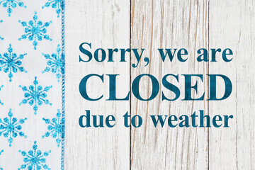 Closed due to weather sign with blue and white snowflakes on with weathered wood