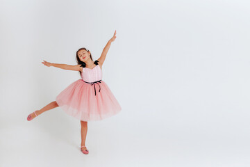 Happy little girl in pink dress dancing on a white background. Space for text. 