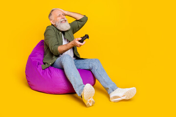 Photo of frustrated mad loser man hold gamepad lose game wear green shirt isolated yellow color background