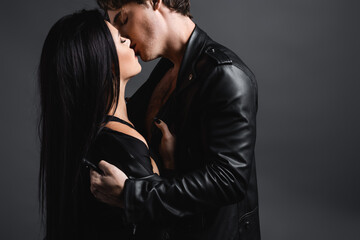 sexy young couple in leather jackets kissing on grey.