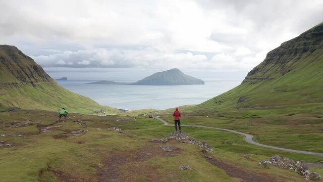 Aerial view of unrecognizable woman looking at the panorama, islands, ocean, green mountain and rock cliffs.Impressions of the fascinating archipelago of the Faroe Islands in the North Atlantic Ocean