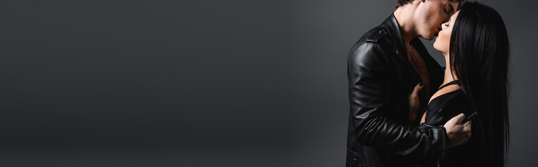 sexy young couple in leather jackets kissing on grey, banner.