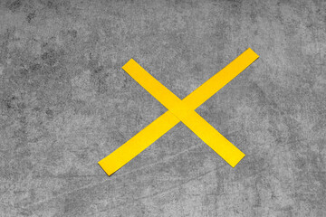 Fototapeta na wymiar on a shabby gray background, two strips of yellow paper in the form of a cross as a forbidding sign; problems of recycling and reuse of paper; vertical photo