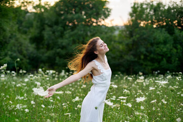 Naklejka na ściany i meble cheerful woman in a field with flowers in a white dress in nature
