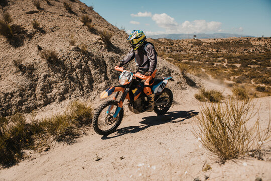 Male biker in protective sportswear riding motorcycle on dirt road
