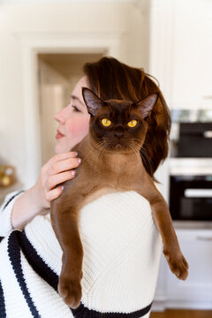 Female pet owner carrying Burmese cat on shoulder at home