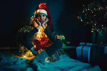 middle-aged blonde woman with a santa hat on her head, tangled in christmas decorations and lights - obrazy, fototapety, plakaty
