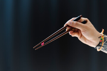 Man holding capsule with chopsticks against black background