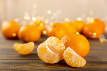 Orange-colored mandarin or clementine fruits with green leaves, on a tree background.