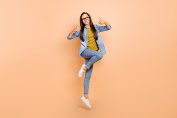 Fototapeta na wymiar Full size photo of pretty female jumping show thumb-up recommending wear denim clothes isolated on beige color background