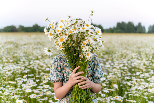 Girl covering face with bunch of flowers at field