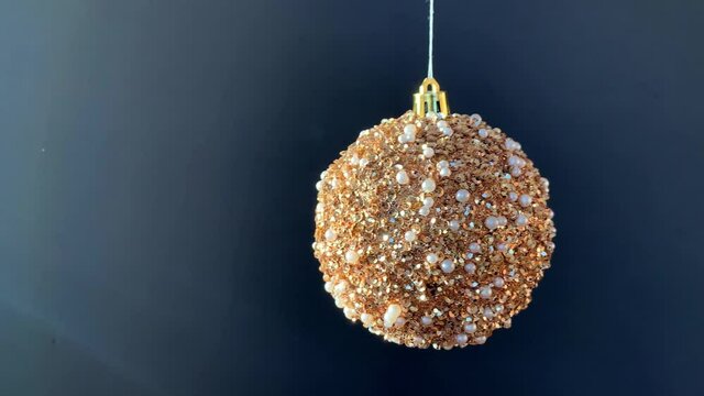 One golden shiny glitter Christmas ball moves and spins on white thread on black background. Free space for your text. New Year decorations