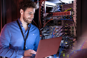 Male IT specialist working on laptop at rack in server room