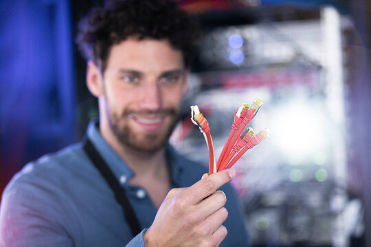 Smiling male IT professional with patch cord cable standing in data center