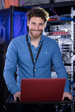 Smiling male IT expertise standing in front of laptop at server room
