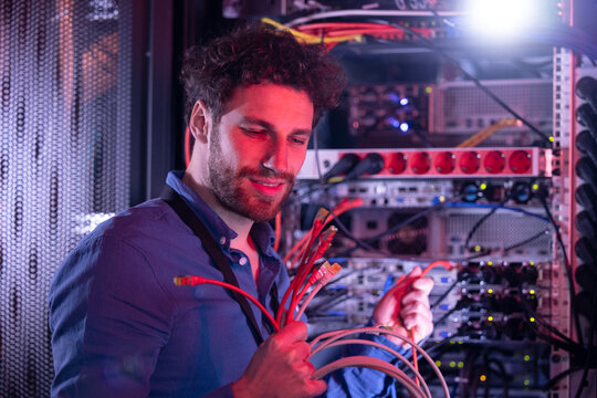 Male IT technician looking at patch cord cables while standing by server rack