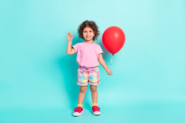 Full size photo of young little girl happy positive smile air balloons wave hello isolated over turquoise color background