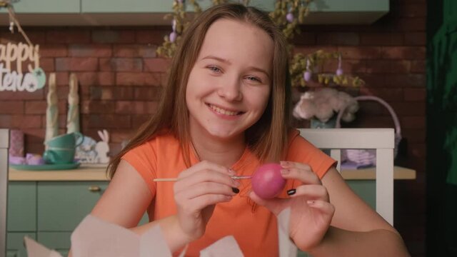 Happy child is painting Easter eggs in the kitchen at home.
