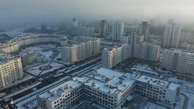 Flight over the city block. Modern multi-storey buildings. Winter cityscape. A misty haze is visible. Aerial photography.