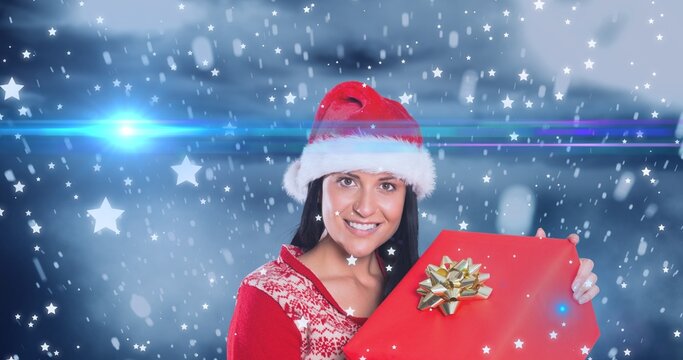 Composition of smiling woman in santa hat with christmas present over snowy background, copy space
