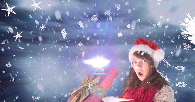 Composition of surprised woman in santa hat with christmas present over snowy background, copy space