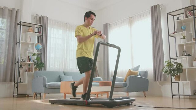 Asian Man Running On A Treadmill And Looking Smart Watch At Home
