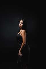 brunette young woman in slip dress standing isolated on black.