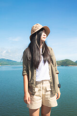 Young happy woman with backpack standing with raised hands and looking to the river. Woman traveling concept