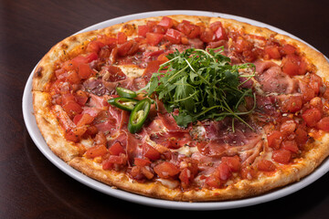 ham pizza with tomatoes, cheese and topped with green chili peppers and arugula