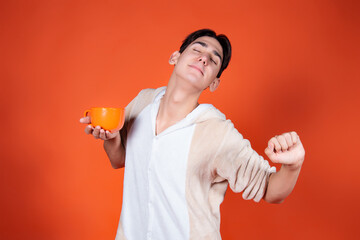 Cheerful man in pajamas with a mug of coffee on an orange background.