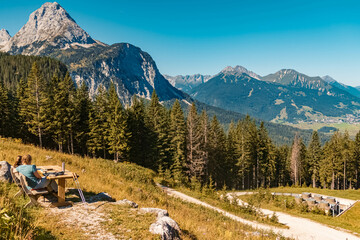 Beautiful alpine summer view with unknown hikers taking a break on a bench at the famous Ehrwalder Alm near Ehrwald, Tyrol, Austria
