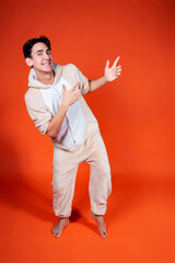 A man in pajamas points with his hands to the side. Guy on an orange background.