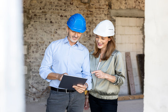 Female client and male architect wearing hardhats while discussing over digital tablet at construction site