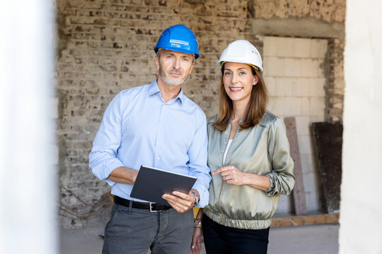 Male architect with digital tablet standing by female client at construction site