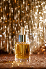 Obraz na płótnie Canvas face oil in glass bottle with silver cap and dropper on rose gold sequin and silver tinsel lametta background . Self care and beauty for the christmas new year holiday season