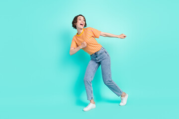 Fototapeta na wymiar Photo of impressed funny young lady wear orange t-shirt dancing smiling isolated turquoise color background