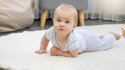 Portrait of cute baby boy with blue eyes lying on soft carpet in house