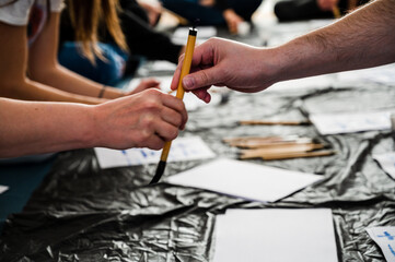 Man and woman supporting each other on art workshop, helping with paintbrush. Close up shot of male's and female's hand touching