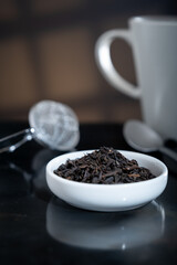 Selective focus closeup of a cup filled with fresh tea leaves. An out-of-focus tea strainer is in the background.