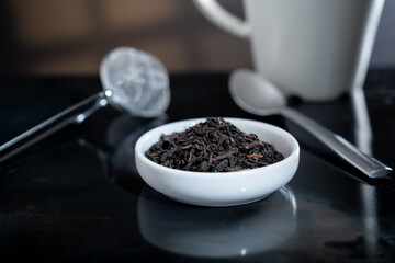 Selective focus closeup of a cup filled with fresh tea leaves. An out-of-focus tea strainer is in the background.